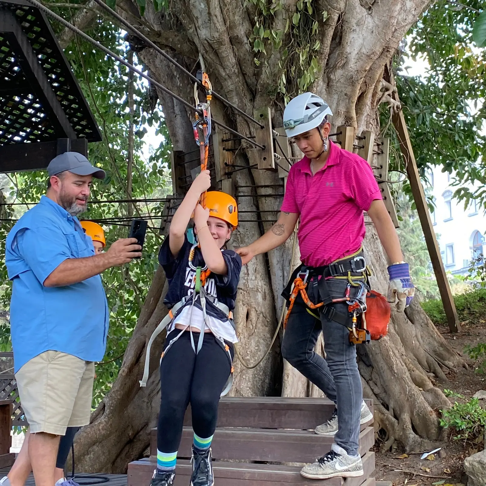 Niña con casco y arnés, colgada de la polea y lista para salir en el canopy, junto al instructor de Vertika