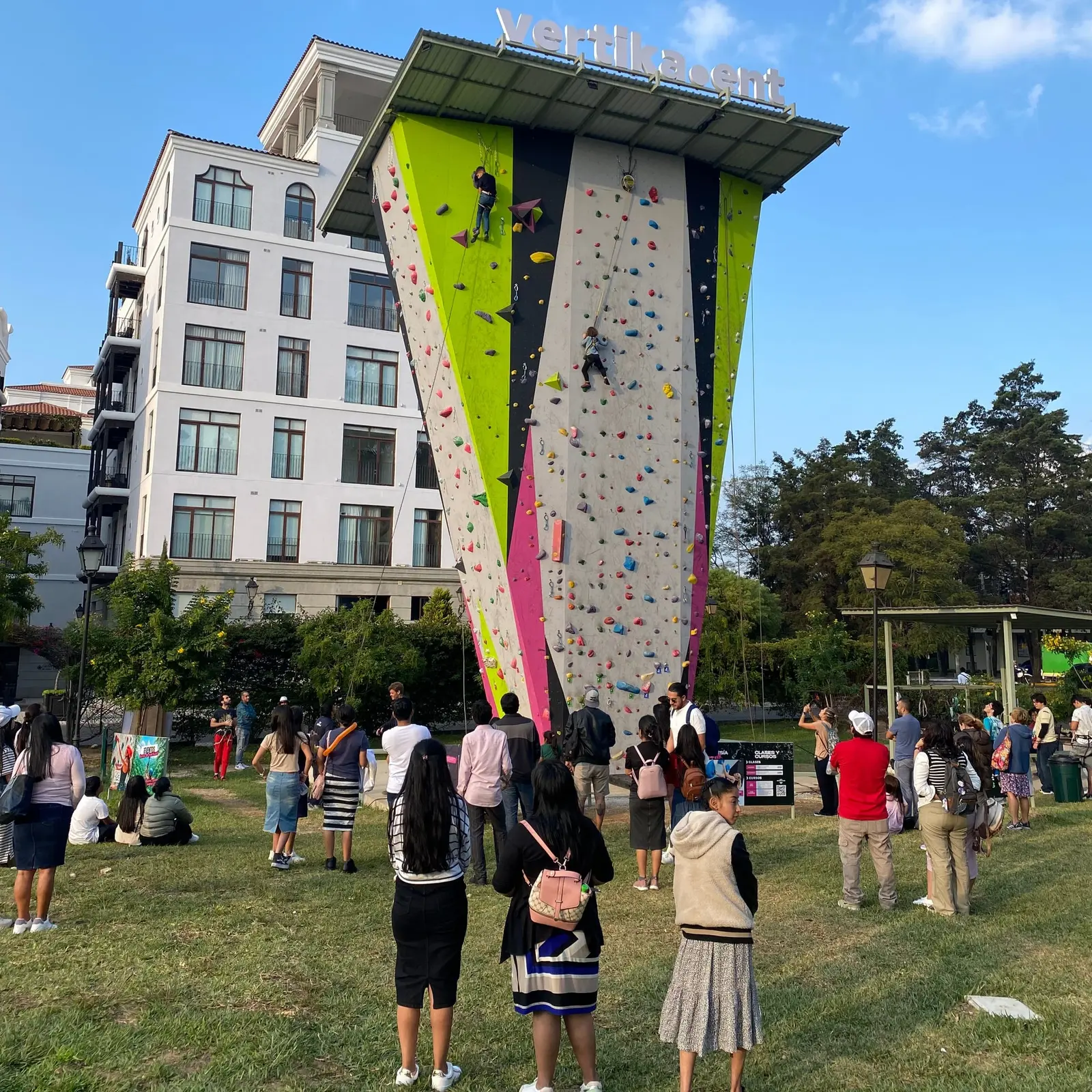 Grupo de personas frente a El Muro, mirando a dos escaladores bajo el letrero de Vertika